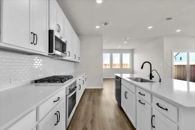a kitchen with white cabinets a sink dishwasher and a stove with wooden floor