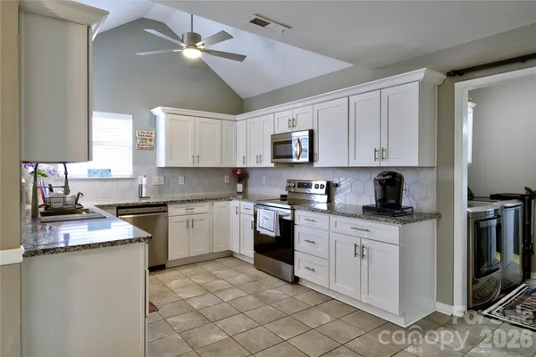a kitchen with stainless steel appliances granite countertop a sink a stove a refrigerator cabinets and a window