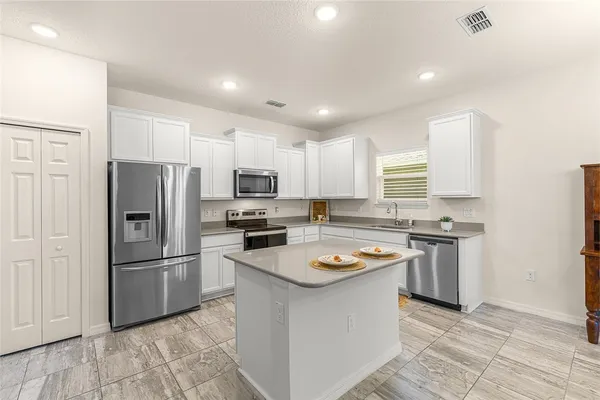 a kitchen with stainless steel appliances granite countertop a refrigerator a sink dishwasher a stove top oven a refrigerator and white cabinets with wooden floor