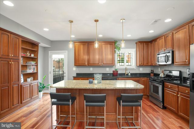 a kitchen with stainless steel appliances granite countertop a stove a sink a microwave a dining table and chairs with wooden floor