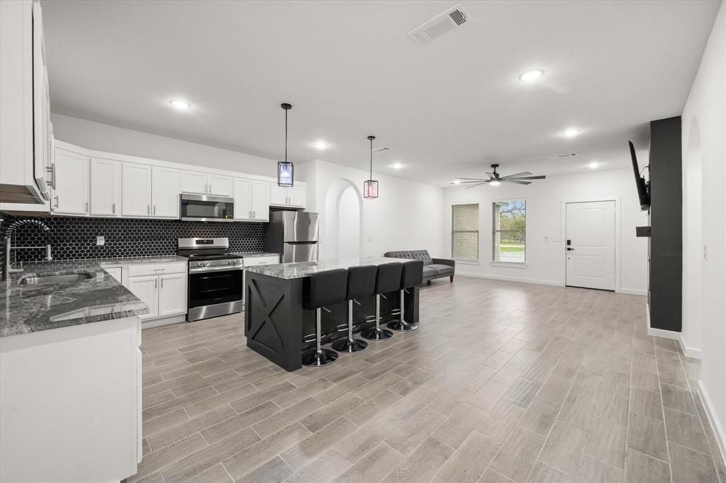 6771 Northwest County Road 1146 Barry, TX 75102 - Photo 19 of 34 a kitchen with stainless steel appliances kitchen island granite countertop a stove a refrigerator a sink a microwave and island with wooden floor