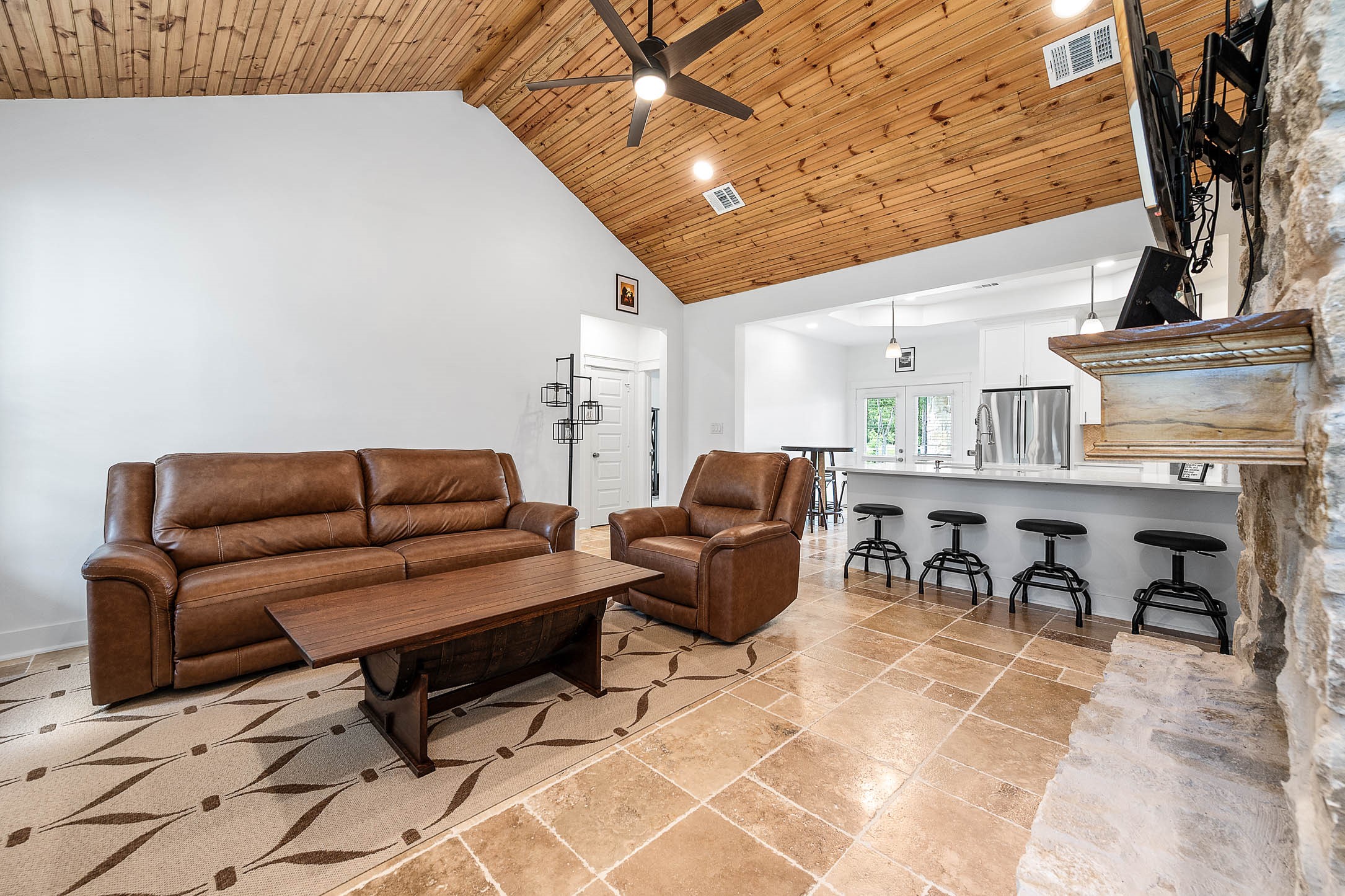 8032 Short Road Needville, TX 77461 - Photo 6 of 50 This open living space showcases vaulted wood-accented ceilings, stylish tile flooring, and a beautiful stone fireplace that serves as the focal point of the room. The seamless flow into the bar-style kitchen with seating makes the space ideal for gathering and entertaining.