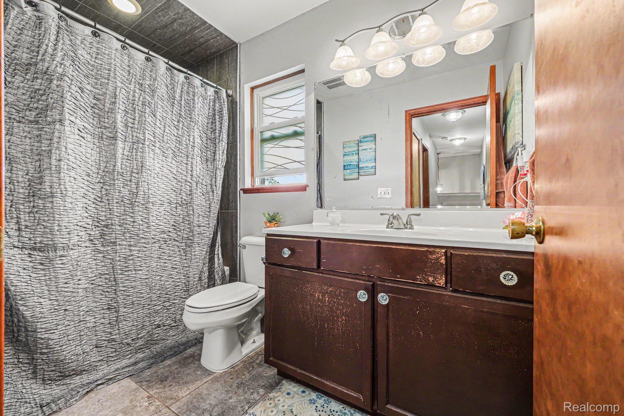 7020 Meldrum Road Fair Haven, MI 48023 - Photo 19 of 43 Bathroom featuring a dark wood-finish vanity with a white countertop and integrated sink, a large mirror, and a multi-light fixture