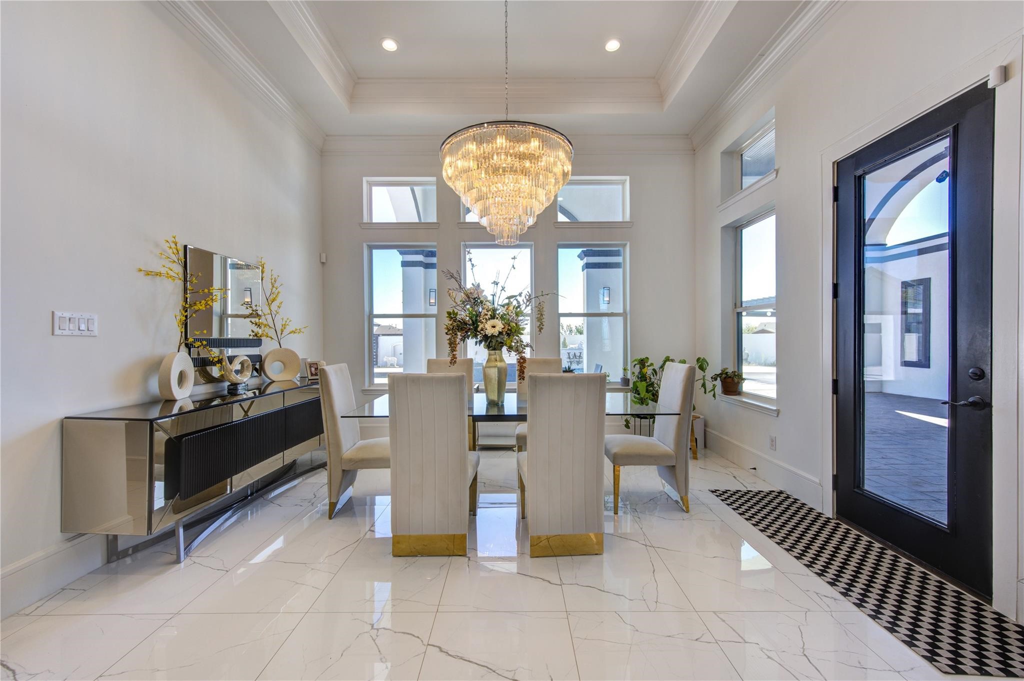 4821 Walters Road Richmond, TX 77469 - Photo 29 of 50 This elegant formal dining room exudes modern luxury with soaring tray ceilings, oversized windows, and a breathtaking multi-tier crystal chandelier serving as the centerpiece of the space. The sleek glass dining table, designer seating with gold accents, and polished marble-style flooring create a sophisticated atmosphere ideal for upscale entertaining. Filled with natural light and finished with refined contemporary touches