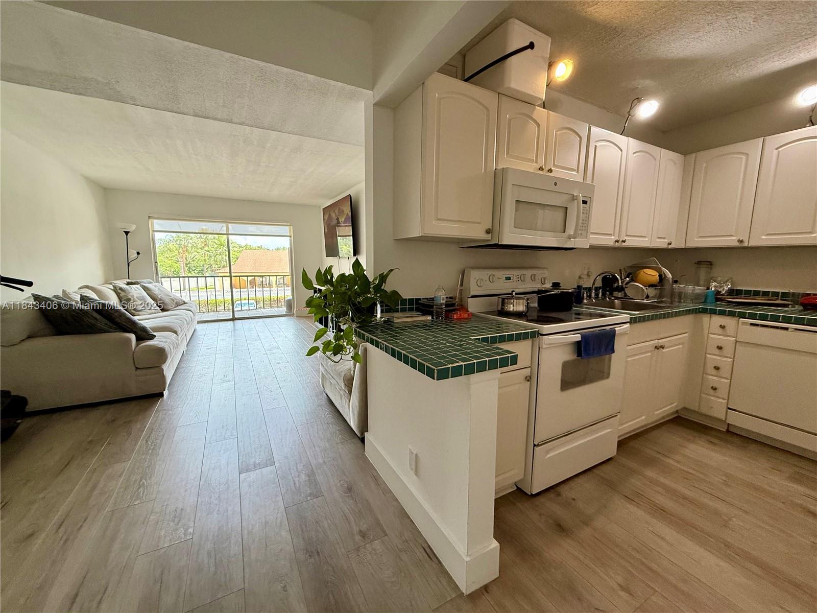 480 Northwest 20th Street, Unit 207 Boca Raton, FL 33431 - Photo 3 of 26 a kitchen with white cabinets a sink dishwasher and a stove with wooden floor