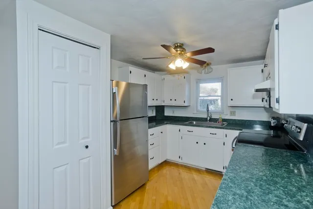 a kitchen with granite countertop a refrigerator a sink a stove and white cabinets