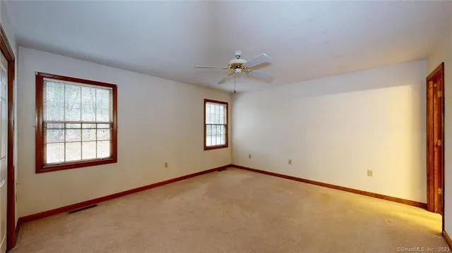an empty room with chandelier fan and windows