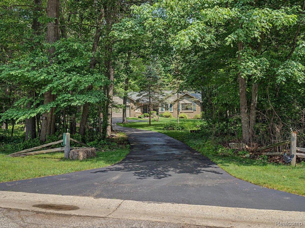 9714 Naiad Road Clarkston, MI 48348 - Photo 59 of 61 A paved driveway leads through a wooded setting toward the brick ranch home, offering a peaceful and private approach from the road.