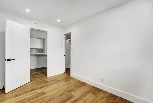 a view of empty room with wooden floor and kitchen