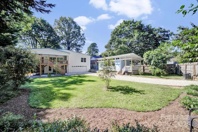a view of a white house in front of a yard with potted plants and large trees