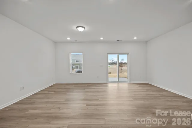 a view of an empty room with wooden floor and windows