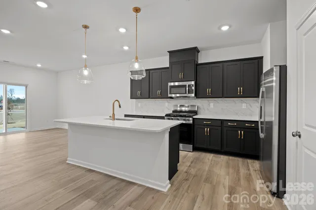 a large kitchen with stainless steel appliances granite countertop a sink a stove a refrigerator and a microwave oven on the wooden floor