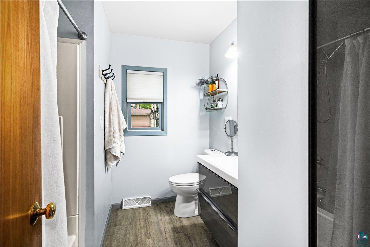 130 West Austin Street Duluth, MN 55803 - Photo 14 of 35 Bathroom featuring wood-finish flooring, a contemporary vanity with white countertop, a toilet, a window with a blind, and a shower area