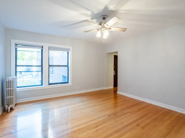 an empty room with wooden floor chandelier fan and windows