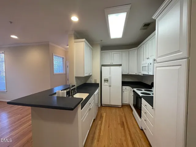 a kitchen with granite countertop a refrigerator a sink dishwasher and a stove top oven with wooden floor