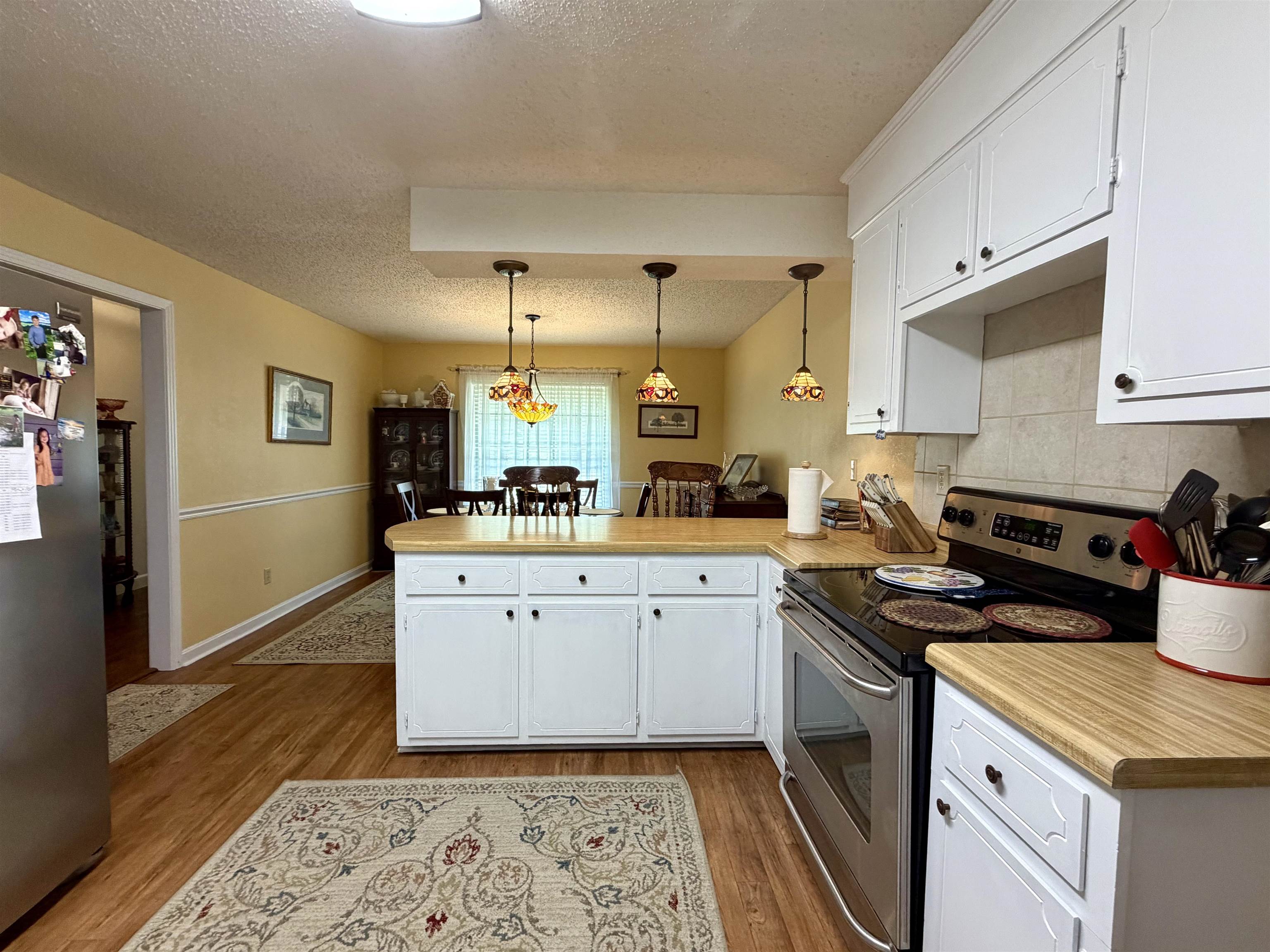 142 Treece Street Selmer, TN 38375 - Photo 6 of 36 Kitchen featuring wood-finish flooring, white cabinetry with black hardware, light wood-look countertops, and a stainless steel range