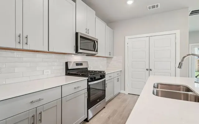 a kitchen with stainless steel appliances granite countertop white cabinets a sink a stove and a refrigerator