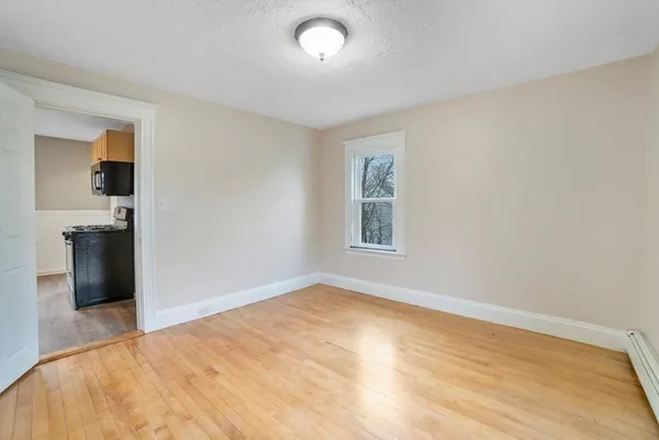 a view of empty room with wooden floor and kitchen view