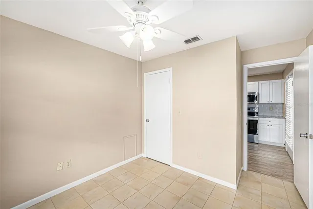 an empty room with kitchen view and a ceiling fan