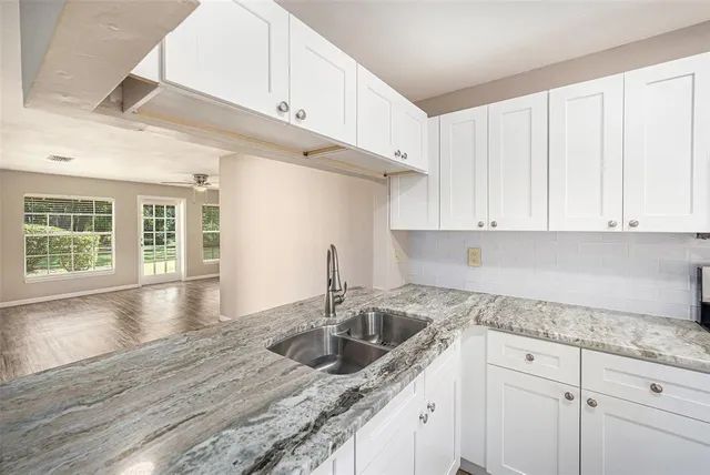 a kitchen with granite countertop a sink stainless steel appliances white cabinets and a window