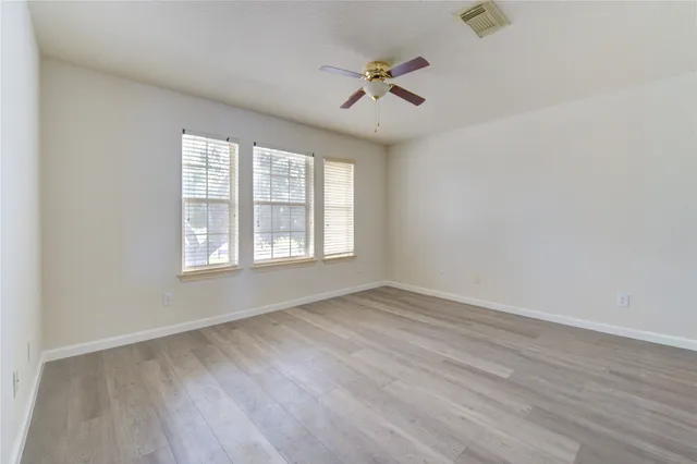 an empty room with wooden floor fan and windows