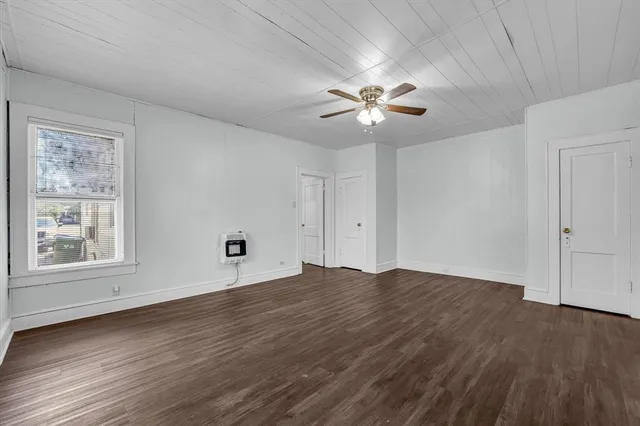 an empty room with wooden floor chandelier fan and windows