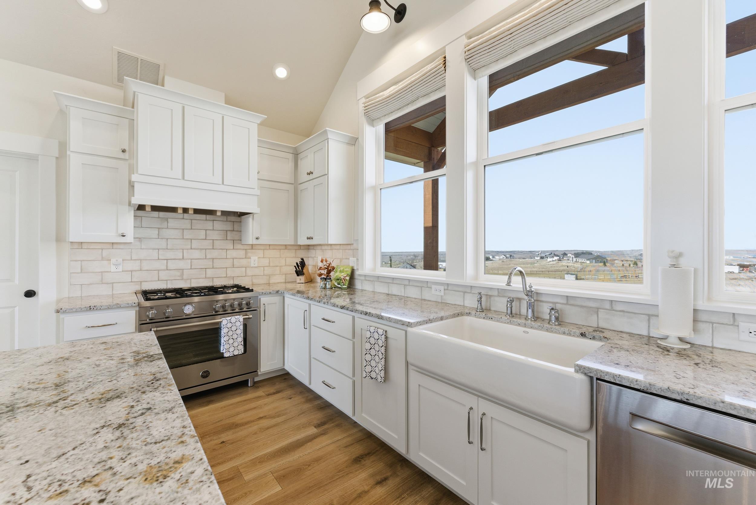 5800 Partridge Peak Avenue Caldwell, ID 83607 - Photo 15 of 50 Kitchen featuring white cabinetry, stainless steel appliances, lofted ceiling, light stone countertops, and light wood-type flooring