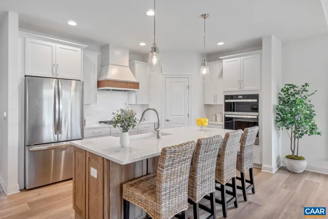 a kitchen with stainless steel appliances granite countertop a refrigerator a sink a stove and chairs with wooden floor