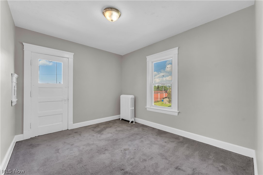 3506 Riverside Avenue Cleveland, OH 44109 - Photo 21 of 31 Room featuring light gray walls, dark gray carpet, white trim, a white four-panel door with a top light, a single window, and a white radiator