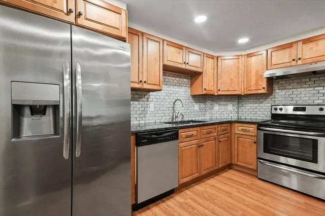 a kitchen with stainless steel appliances granite countertop a refrigerator a sink and white cabinets
