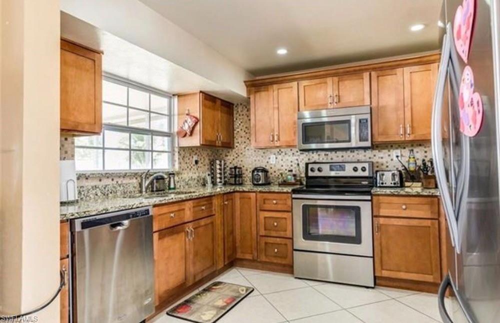 5325 23rd Place Southwest Naples, FL 34116 - Photo 2 of 10 Kitchen featuring light wood cabinetry, stainless steel appliances, a window above the sink, granite countertops, and a tiled backsplash