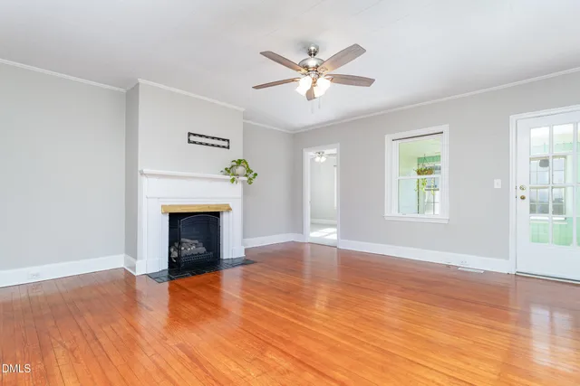 a view of an empty room with wooden floor fireplace and a window