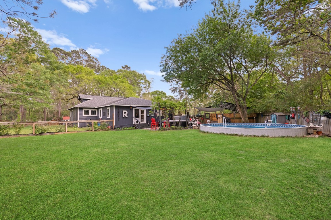 10960 McDowell Road Conroe, TX 77306 - Photo 22 of 25 Wide view of the backyard showcasing the home, pool, and expansive green space—perfect for outdoor living and entertaining.