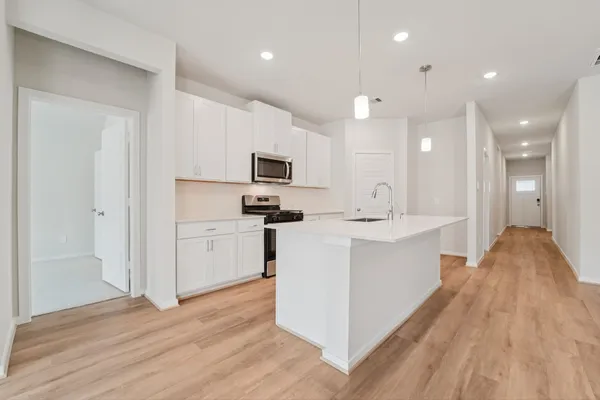 a large white kitchen with a stove a sink dishwasher and a refrigerator with wooden floor