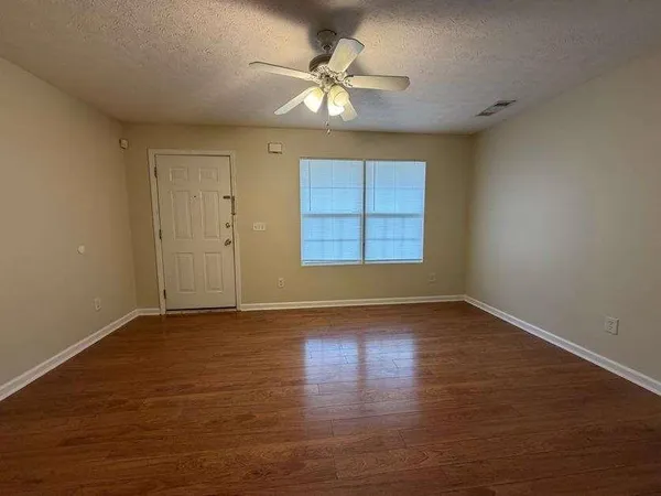 an empty room with wooden floor chandelier fan and windows