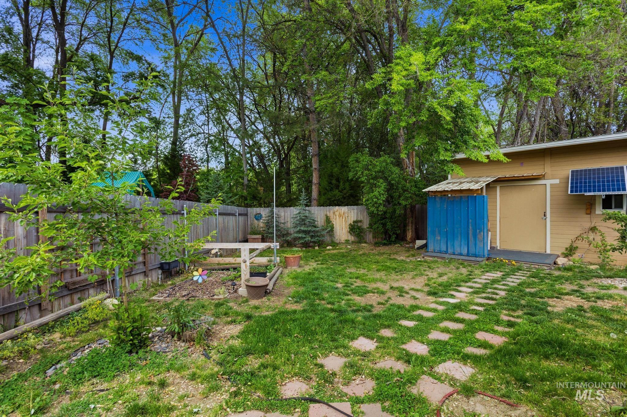 3040 West Hester Street Boise, ID 83702 - Photo 20 of 20 Expansive grassy area with stepping stones leading to a building featuring a tan exterior, a blue side structure, and a solar panel array