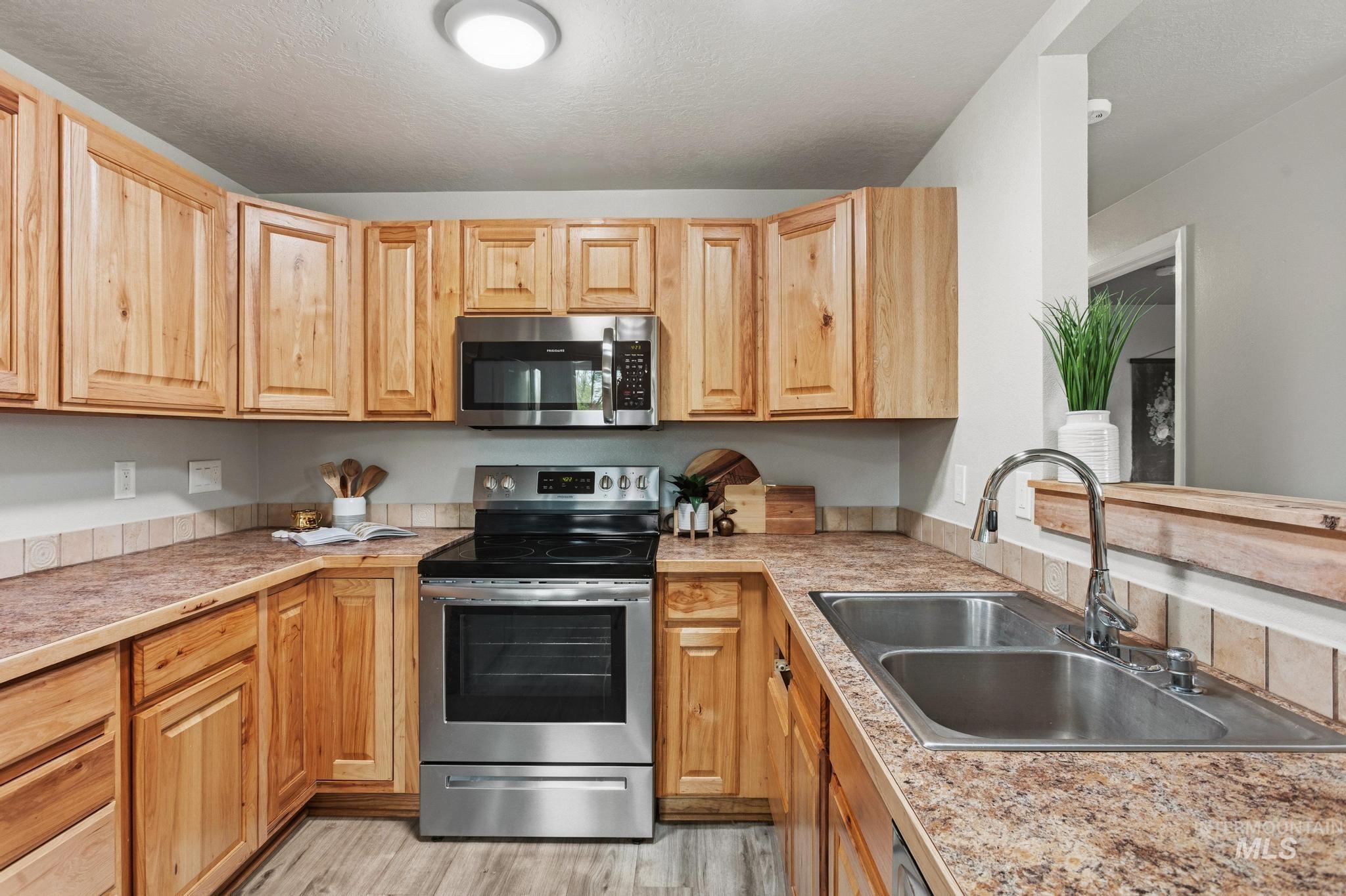 3040 West Hester Street Boise, ID 83702 - Photo 9 of 20 U-shaped kitchen featuring wood cabinetry, stainless steel appliances, laminate countertops, a tile backsplash, and a double basin stainless steel sink with a pull-down faucet