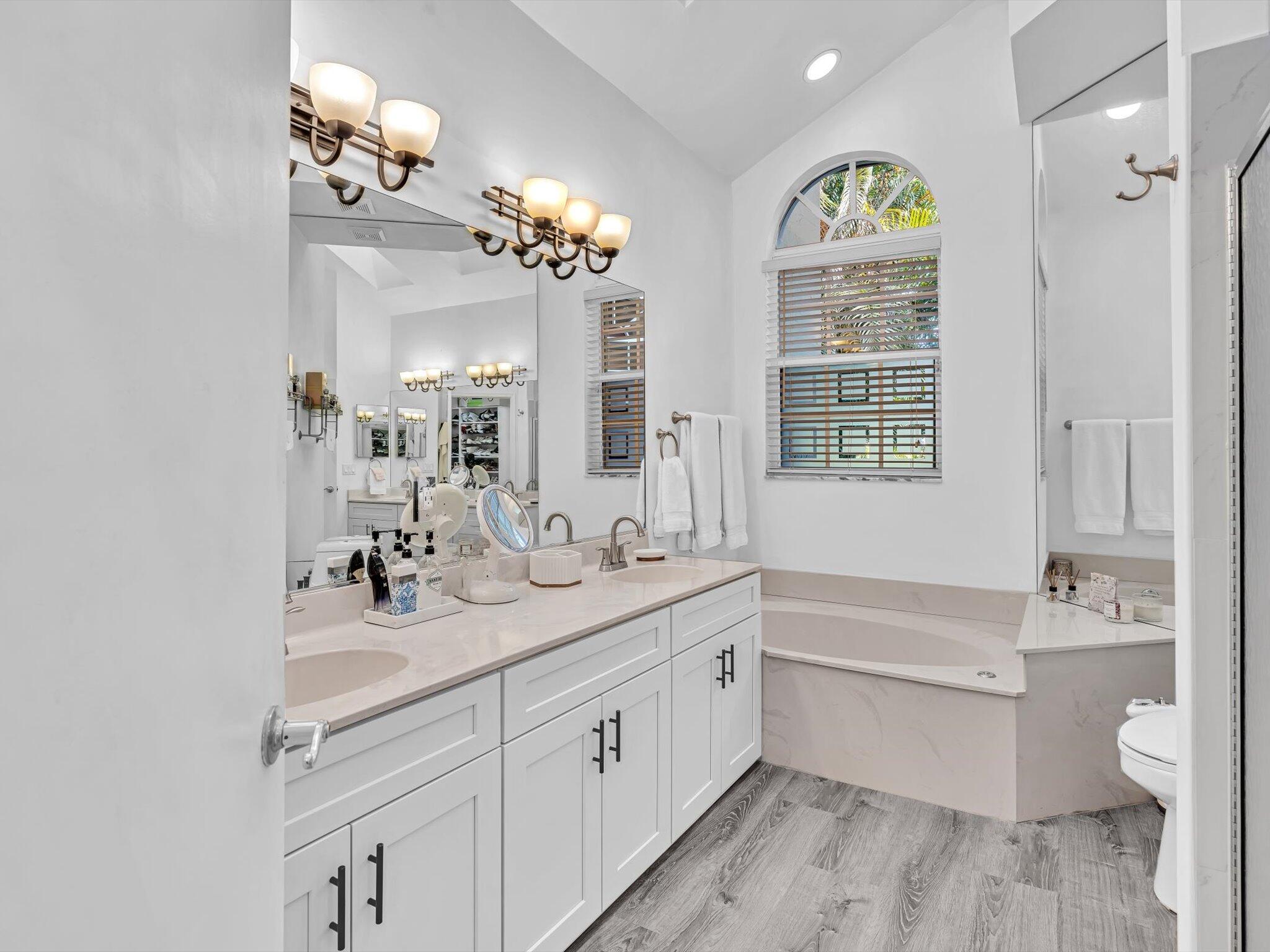2486 Northwest 66th Drive Boca Raton, FL 33496 - Photo 17 of 80 a bathroom with a double vanity sink a large mirror a bathtub and a window