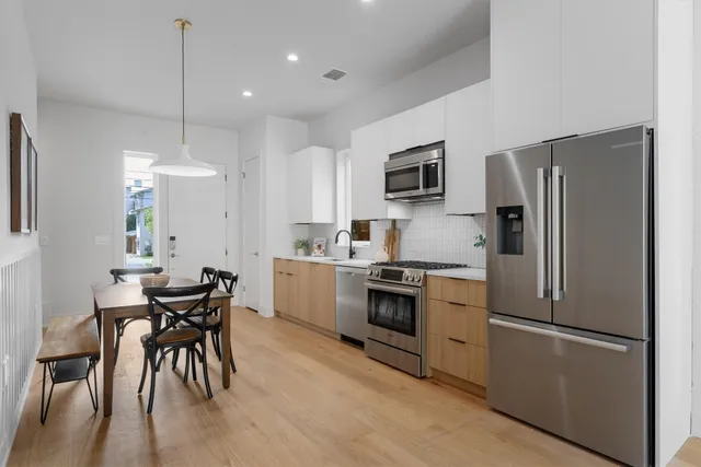 a kitchen with stainless steel appliances granite countertop a refrigerator a stove a sink a dining table and chairs with wooden floor