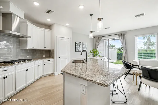 a kitchen with kitchen island granite countertop a table chairs in it wooden floors and white cabinets