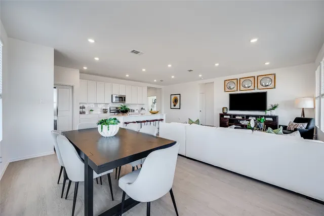 a living room with stainless steel appliances a table and chairs in it