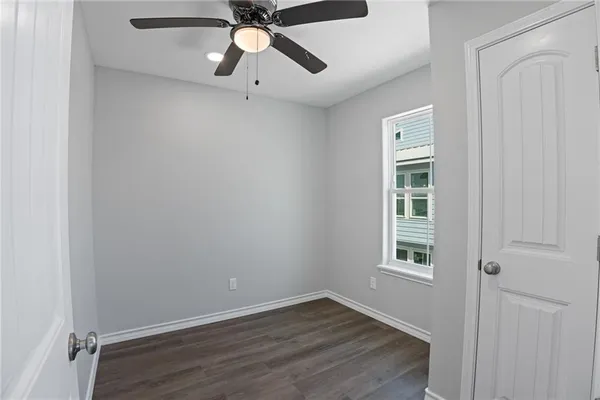 an empty room with wooden floor chandelier fan and windows