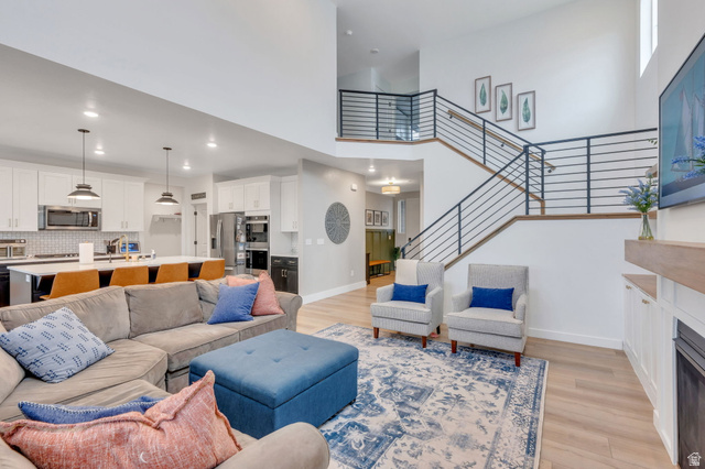 Open-concept living space with high ceilings, wood-finish flooring, and a modern staircase featuring horizontal iron railings