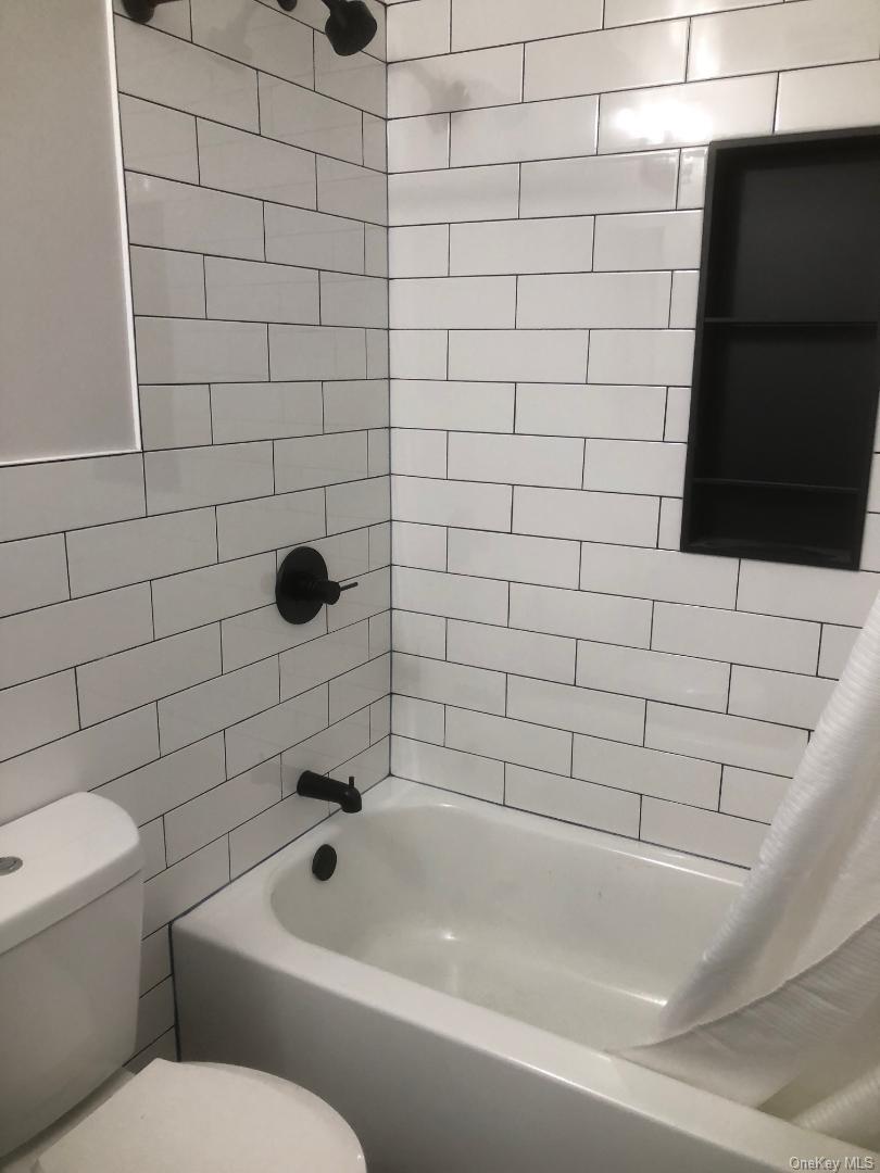 85 North Middletown Road, Unit D10 Nanuet, NY 10954 - Photo 10 of 12 Bathroom featuring white subway tile surround with dark grout, built-in black shower niche, matte black shower fixtures, and a white bathtub