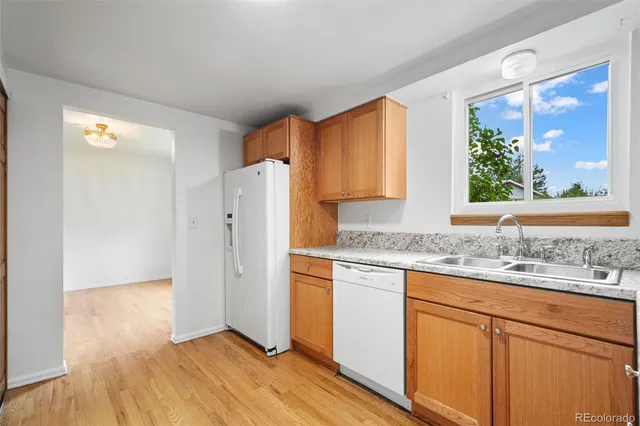 a kitchen with stainless steel appliances granite countertop a refrigerator a sink and white cabinets with wooden floor