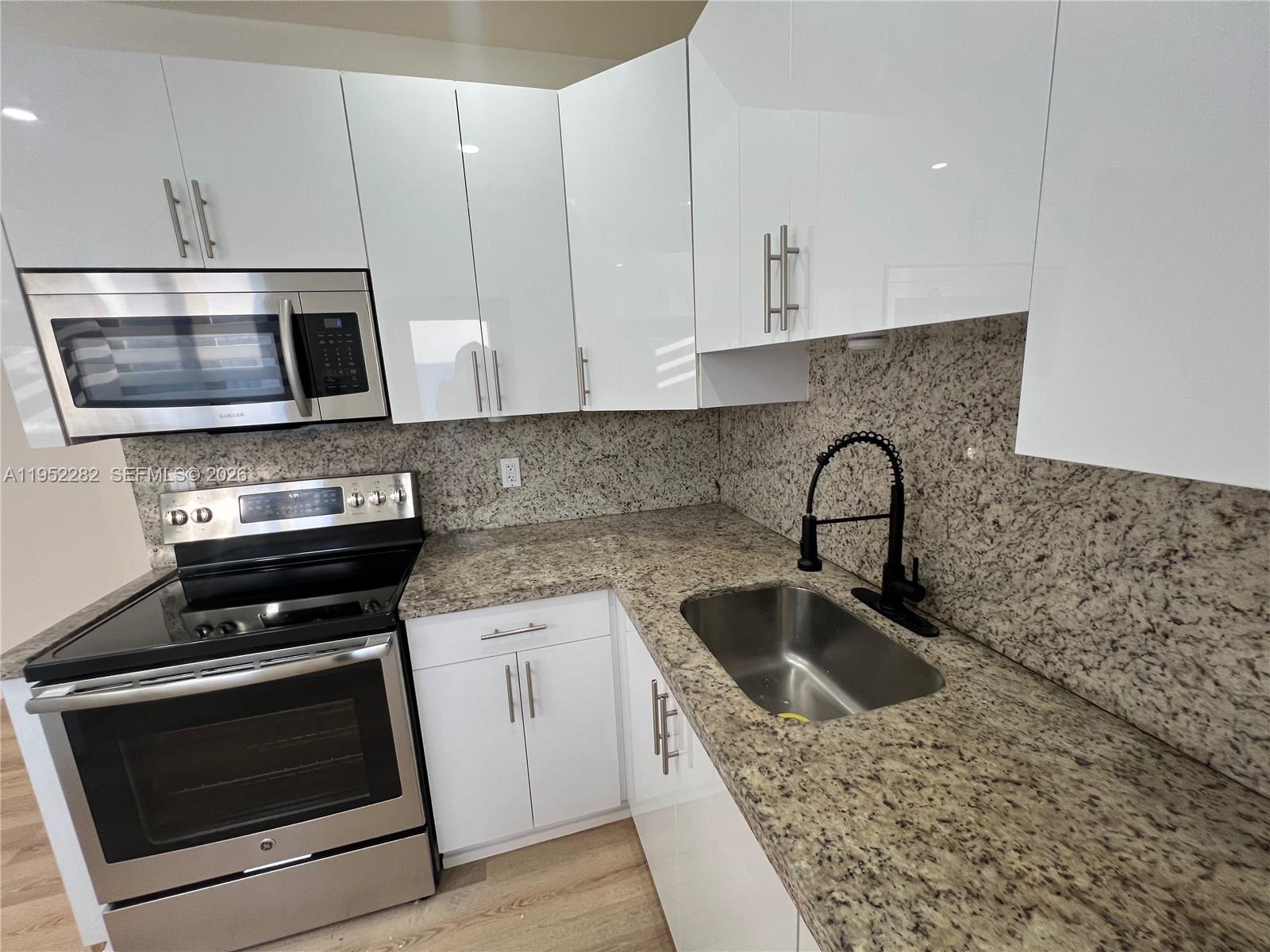 3297 Southwest 26th Street, Unit 3297 Miami, FL 33133 - Photo 7 of 20 a kitchen with granite countertop a sink stainless steel appliances and white cabinets