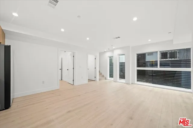 a view of an empty room with kitchen and entryway