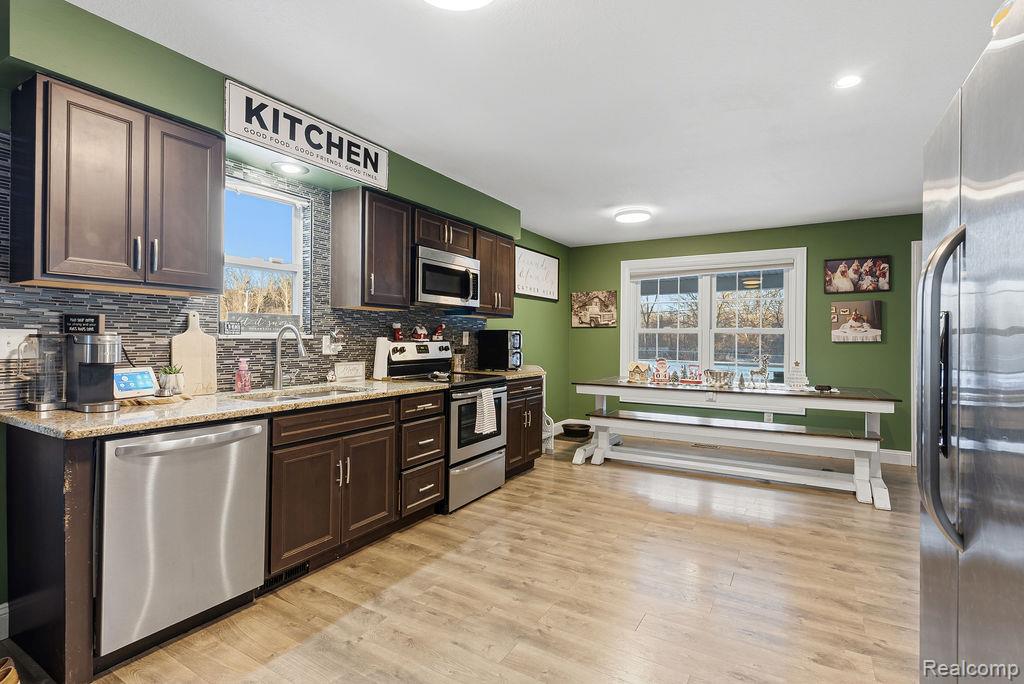 5216 South State Road Goodrich, MI 48438 - Photo 11 of 52 Kitchen featuring dark brown cabinetry, appliances with stainless steel finishes, light stone countertops, tasteful backsplash, and light wood finished floors