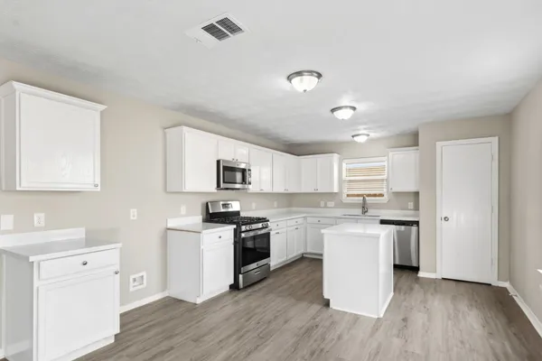 a kitchen with stainless steel appliances a stove top oven a sink a refrigerator a white cabinets and wooden floor