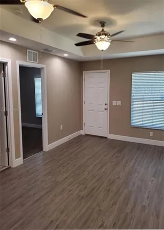 a view of an empty room with wooden floor and a ceiling fan